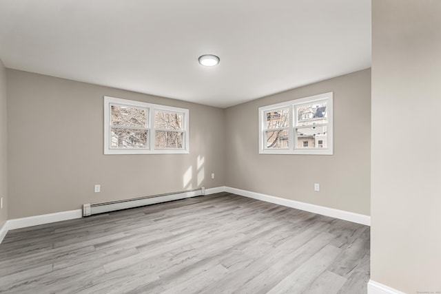 empty room with baseboard heating, a healthy amount of sunlight, and light hardwood / wood-style flooring