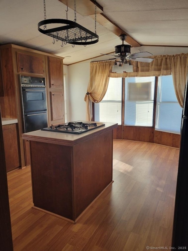 kitchen featuring lofted ceiling with beams, light wood-style flooring, dobule oven black, a kitchen island, and stainless steel gas stovetop