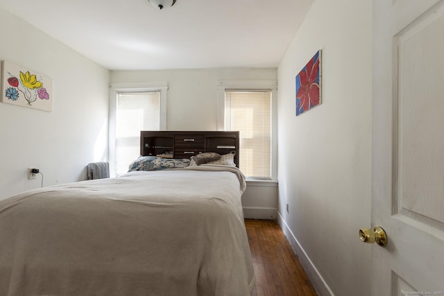 bedroom with multiple windows, radiator heating unit, and dark hardwood / wood-style flooring