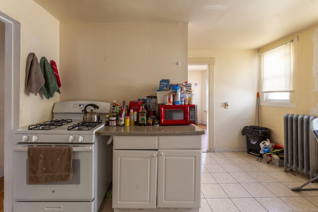 kitchen with light tile patterned flooring, white gas range, radiator heating unit, and white cabinets