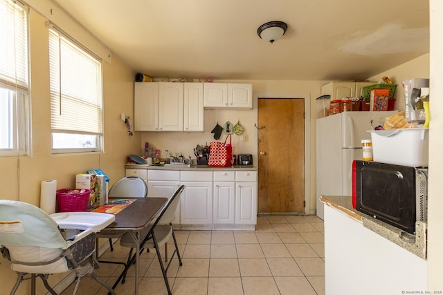 kitchen with light tile patterned flooring, a wealth of natural light, white fridge, and white cabinets