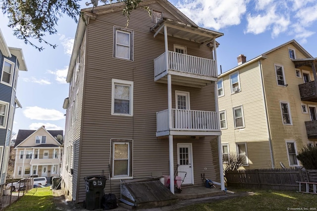 rear view of property featuring a balcony and a yard