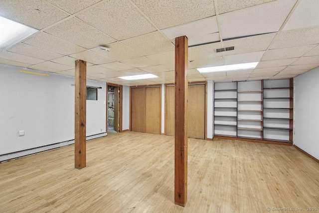 basement featuring a paneled ceiling, wood-type flooring, and a baseboard heating unit