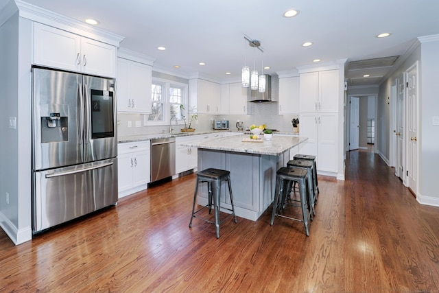 kitchen with white cabinetry, decorative light fixtures, appliances with stainless steel finishes, a kitchen island, and wall chimney range hood