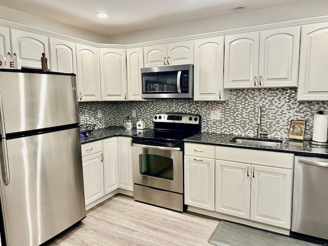 kitchen with appliances with stainless steel finishes, white cabinetry, sink, dark stone countertops, and light hardwood / wood-style floors