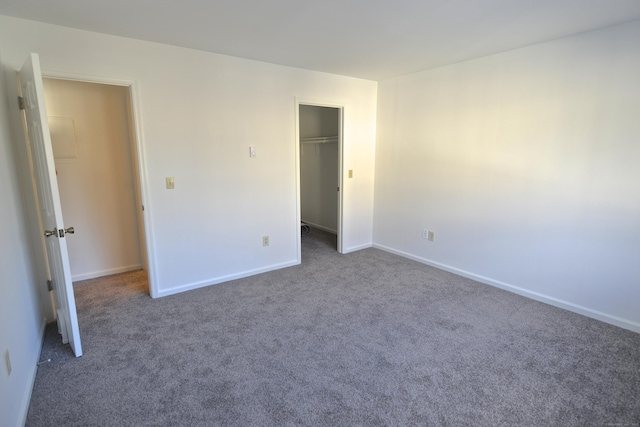 unfurnished bedroom featuring a spacious closet, a closet, and dark colored carpet