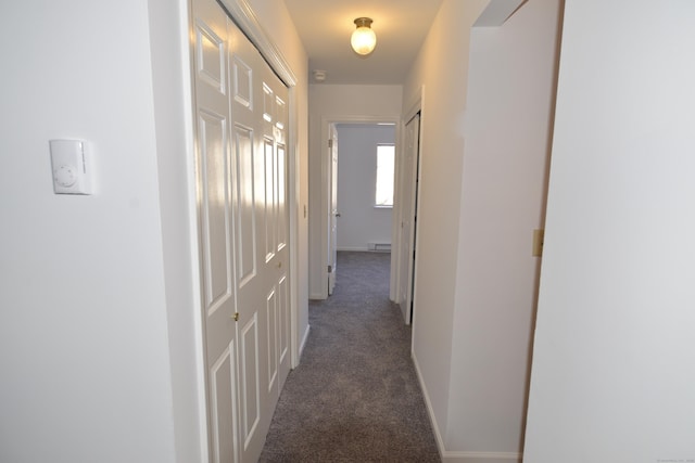 corridor with dark carpet and a baseboard heating unit