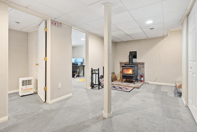 basement featuring a drop ceiling, light colored carpet, and a wood stove