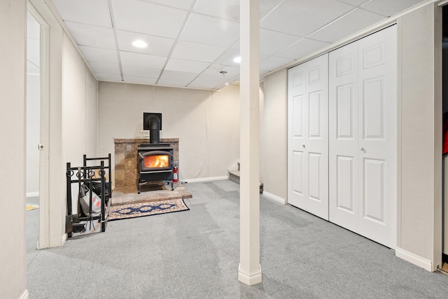 basement with a drop ceiling, a wood stove, and carpet flooring