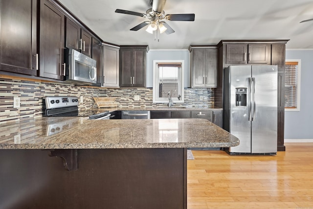 kitchen featuring a kitchen bar, sink, kitchen peninsula, stone counters, and stainless steel appliances