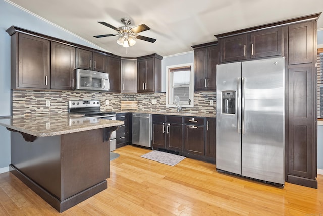 kitchen with vaulted ceiling, appliances with stainless steel finishes, sink, kitchen peninsula, and light stone countertops