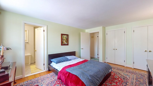 bedroom featuring connected bathroom, two closets, and light hardwood / wood-style flooring