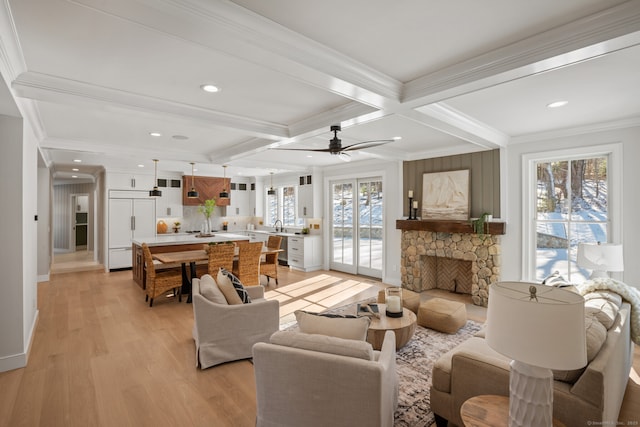 living room featuring a stone fireplace, beamed ceiling, coffered ceiling, light hardwood / wood-style floors, and crown molding