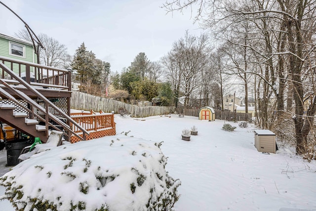 snowy yard featuring a storage shed and a deck