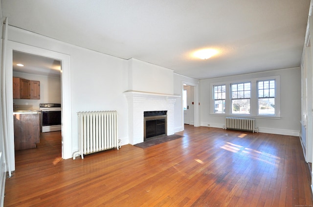 unfurnished living room with radiator heating unit, a fireplace, and hardwood / wood-style floors