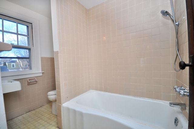 bathroom featuring toilet, tiled shower / bath combo, tile patterned flooring, and tile walls