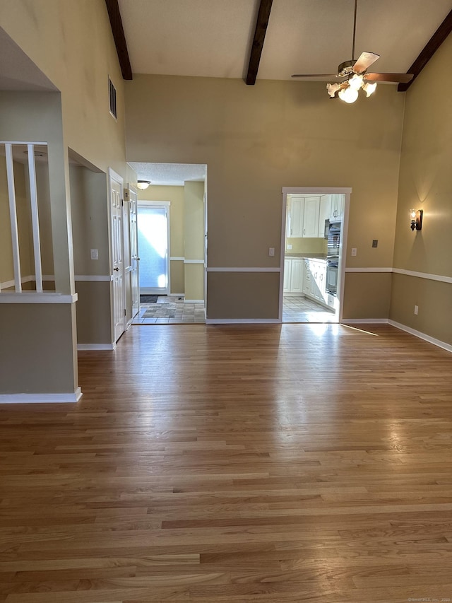 interior space featuring beam ceiling, light hardwood / wood-style flooring, ceiling fan, and a towering ceiling