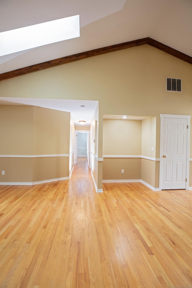 empty room with vaulted ceiling with beams and light hardwood / wood-style flooring