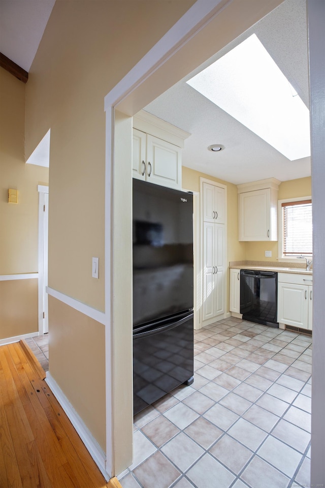 kitchen with a skylight, sink, white cabinets, light tile patterned floors, and black appliances