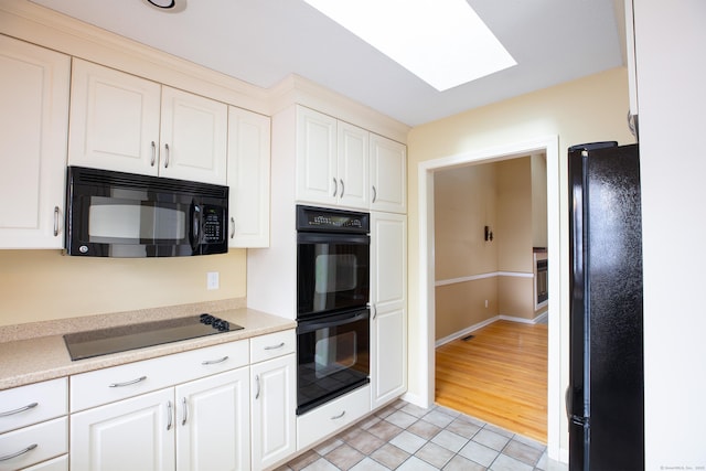 kitchen with white cabinetry, a skylight, black appliances, and light tile patterned flooring