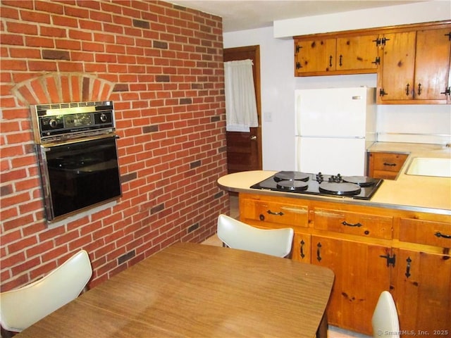 kitchen with sink, white refrigerator, brick wall, black gas cooktop, and oven