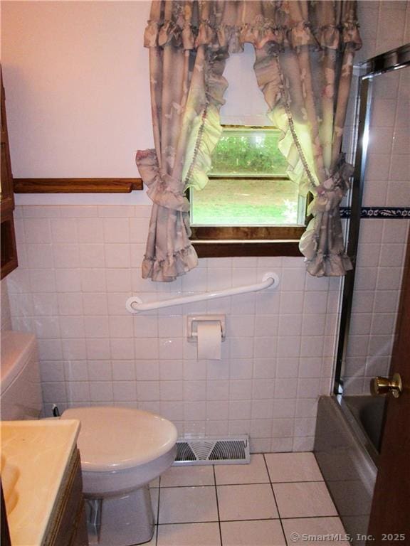 full bathroom featuring bath / shower combo with glass door, tile walls, tile patterned flooring, vanity, and toilet