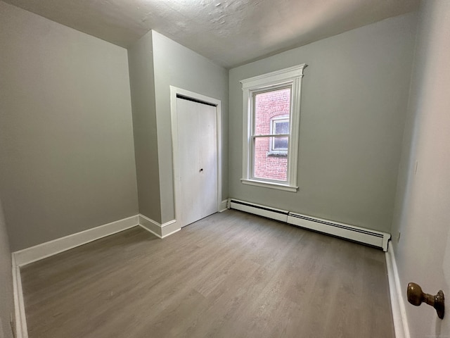 unfurnished room featuring a baseboard heating unit, a textured ceiling, and light hardwood / wood-style floors