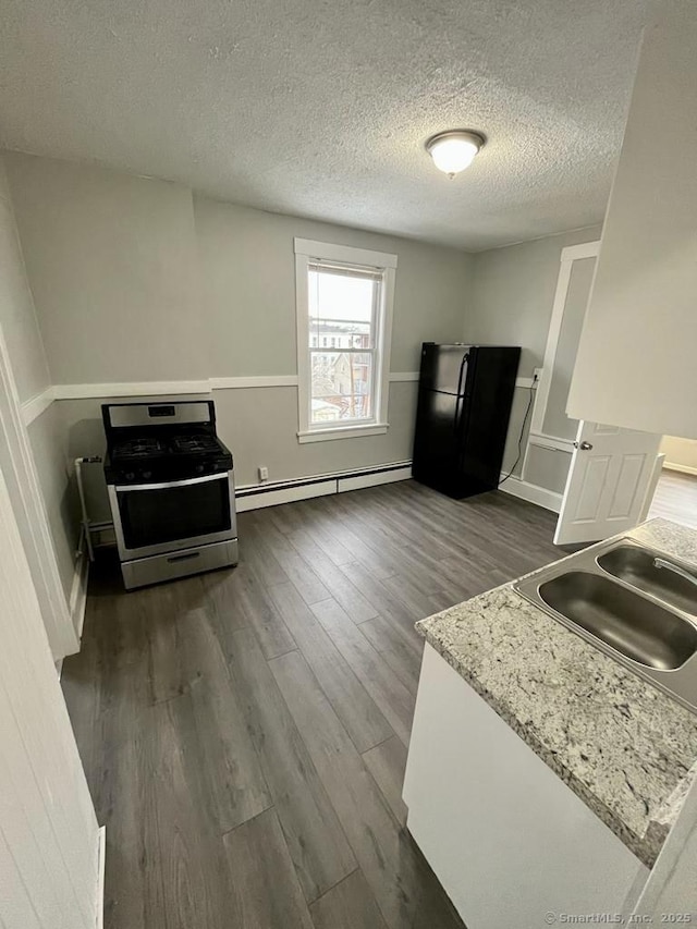 kitchen featuring black refrigerator, sink, baseboard heating, light stone countertops, and stainless steel gas range