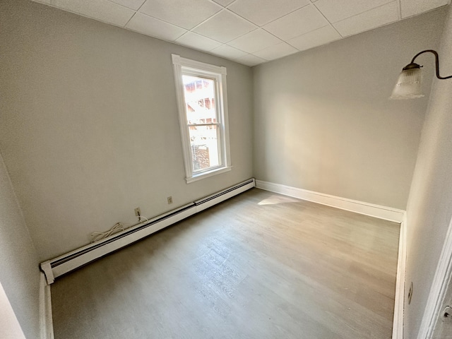 empty room with a drop ceiling, a baseboard radiator, and light wood-type flooring