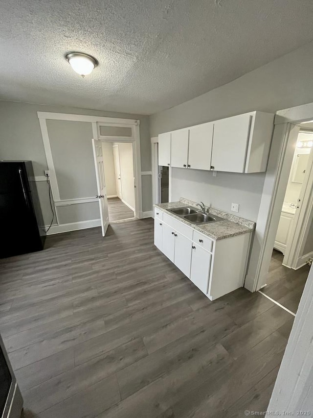 kitchen with sink, dark wood-type flooring, a textured ceiling, white cabinets, and black fridge