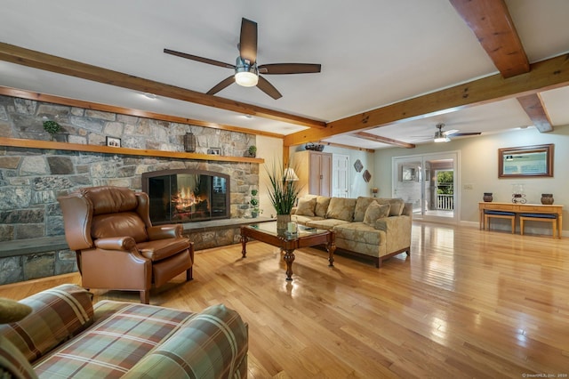 living room featuring beam ceiling, a stone fireplace, ceiling fan, and light wood-type flooring