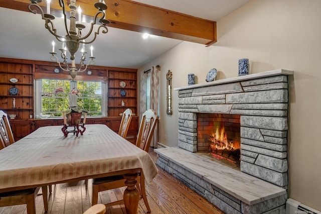 dining space with a stone fireplace, beamed ceiling, an inviting chandelier, a baseboard radiator, and hardwood / wood-style flooring