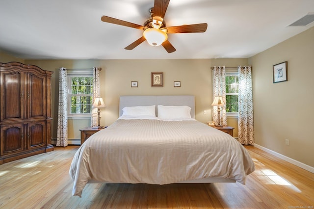 bedroom featuring multiple windows, light wood-type flooring, ceiling fan, and baseboard heating