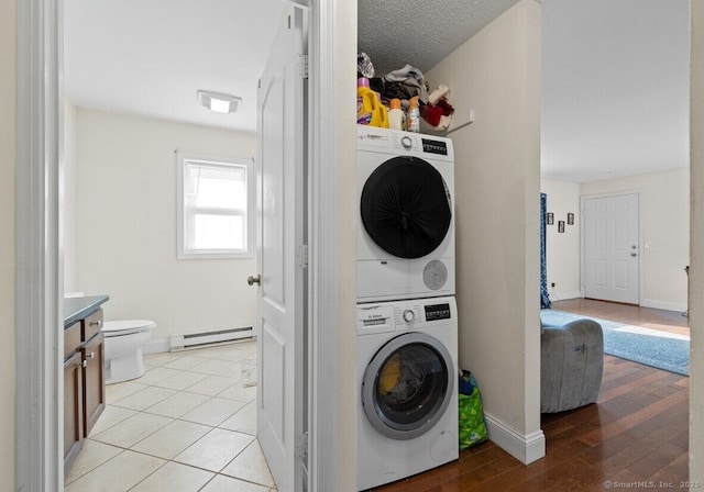 washroom with stacked washer and dryer, light tile patterned floors, a textured ceiling, and baseboard heating