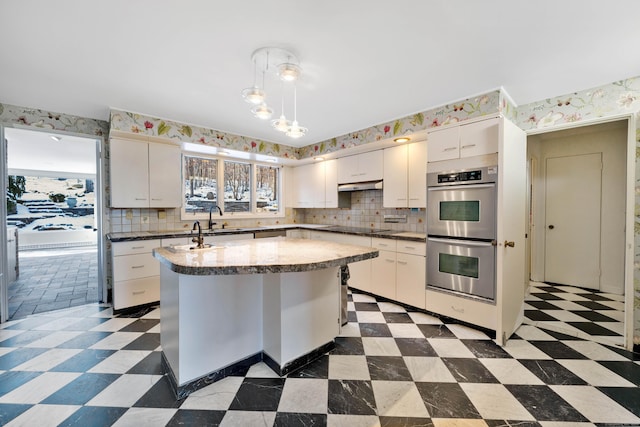 kitchen featuring light floors, stainless steel double oven, white cabinets, and pendant lighting