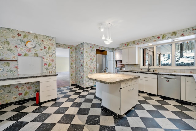 kitchen featuring dark floors, stainless steel appliances, white cabinets, a kitchen island, and wallpapered walls