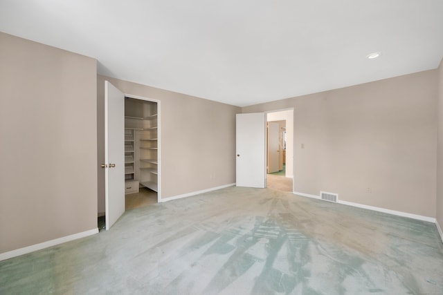 unfurnished bedroom featuring light carpet, baseboards, visible vents, and a walk in closet