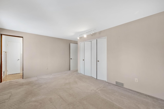 unfurnished bedroom with track lighting, a closet, visible vents, and light colored carpet