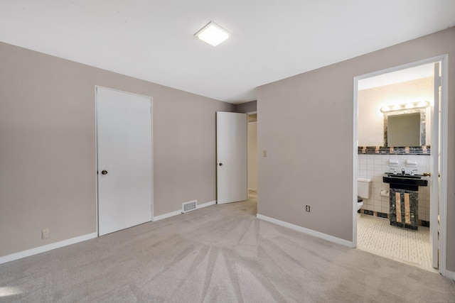 unfurnished bedroom with visible vents, connected bathroom, light carpet, and baseboards