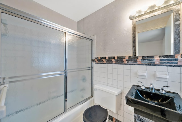 bathroom with a textured wall, toilet, shower / bath combination with glass door, a sink, and tile walls