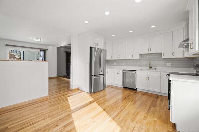 kitchen with appliances with stainless steel finishes, white cabinetry, sink, backsplash, and light hardwood / wood-style flooring