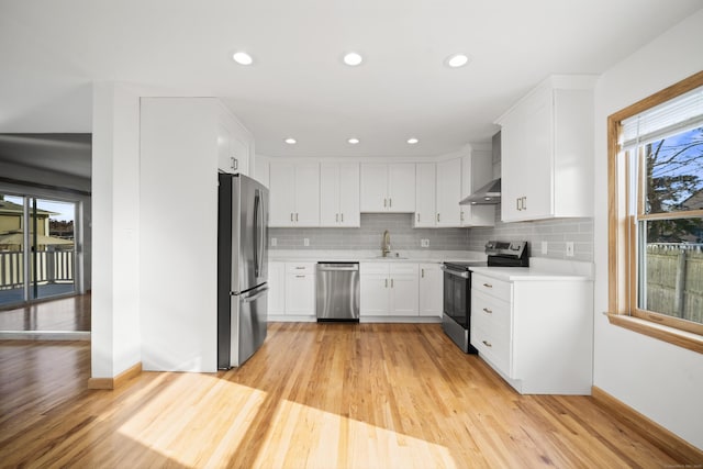 kitchen featuring backsplash, white cabinets, stainless steel appliances, light wood-type flooring, and wall chimney exhaust hood