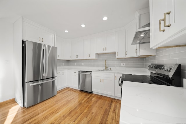 kitchen with appliances with stainless steel finishes, sink, white cabinets, exhaust hood, and light hardwood / wood-style flooring