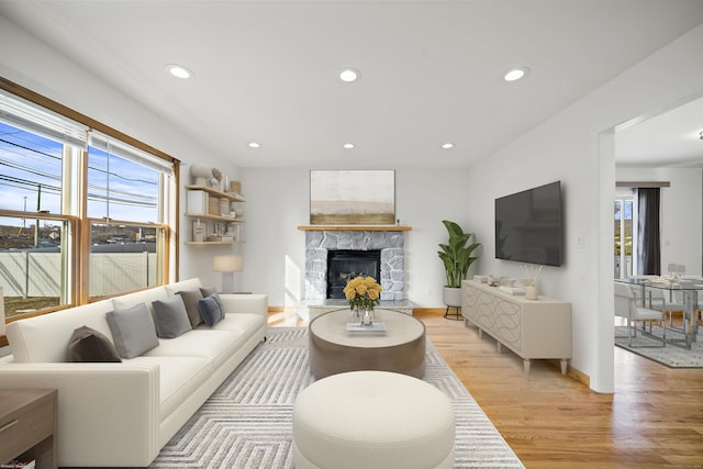 living room featuring a healthy amount of sunlight, a stone fireplace, and light hardwood / wood-style floors