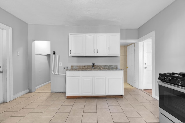 kitchen with white cabinetry, sink, dark stone countertops, light tile patterned floors, and gas range