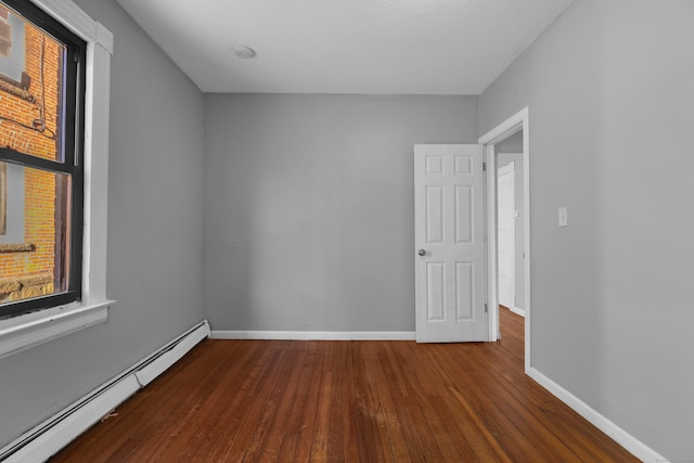 unfurnished room featuring a baseboard heating unit and hardwood / wood-style floors