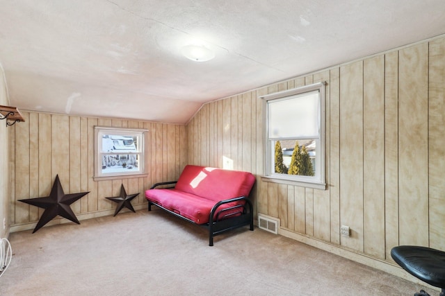 living area with vaulted ceiling, light colored carpet, and wooden walls