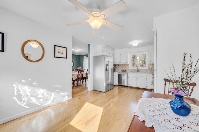 kitchen featuring appliances with stainless steel finishes, sink, white cabinets, backsplash, and light hardwood / wood-style flooring