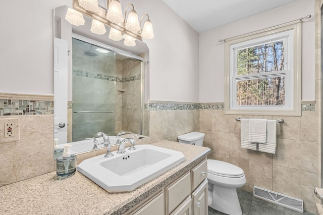 bathroom with tile walls, vanity, toilet, a shower with door, and tile patterned floors