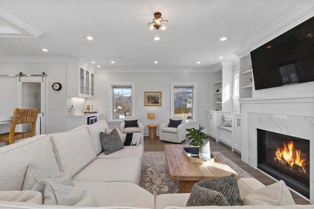 living room with dark hardwood / wood-style flooring, ornamental molding, a high end fireplace, a barn door, and built in shelves